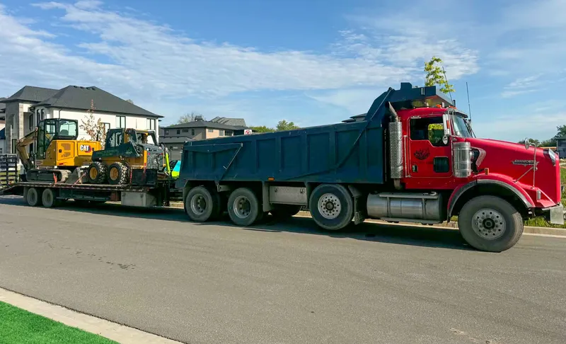 Legacy Exteriors dump truck hauling a mini excavator and skid steer to a job site in Windsor