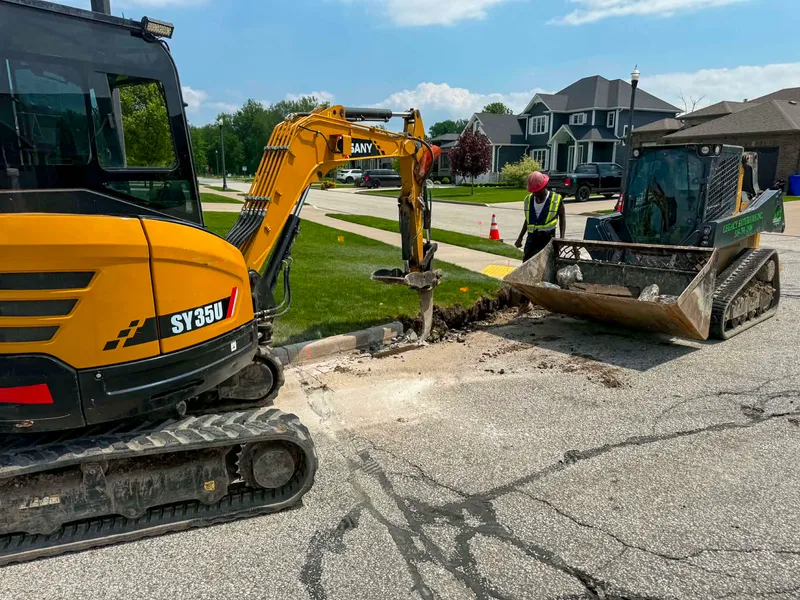 SANY excavator and skid steer trenching at the curb in a residential neighbourhood