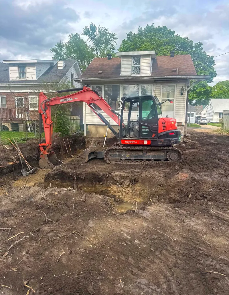 Kubota excavator digging footing trenches beside a home