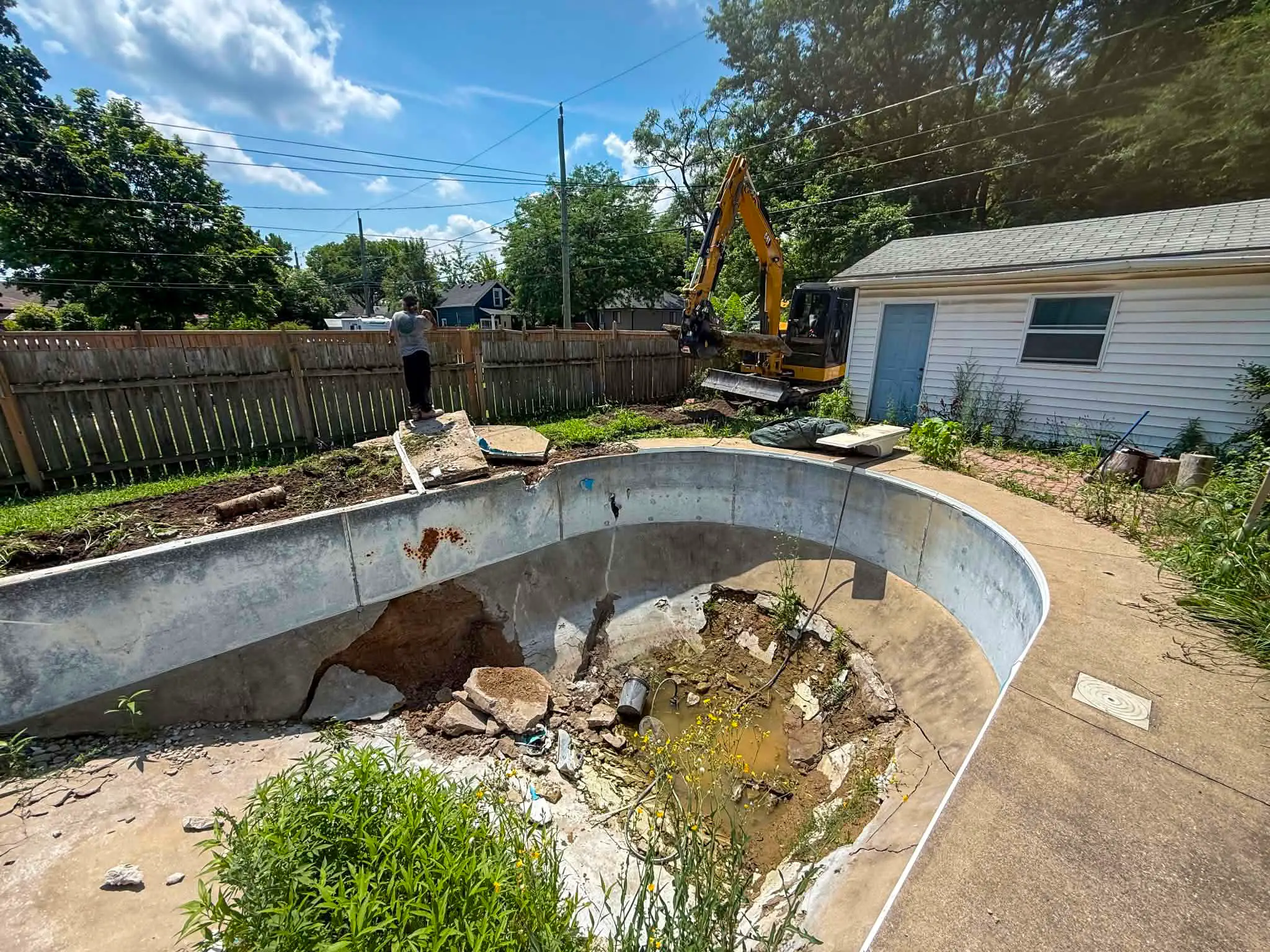 Excavator beginning complete pool removal, breaking up the concrete deck